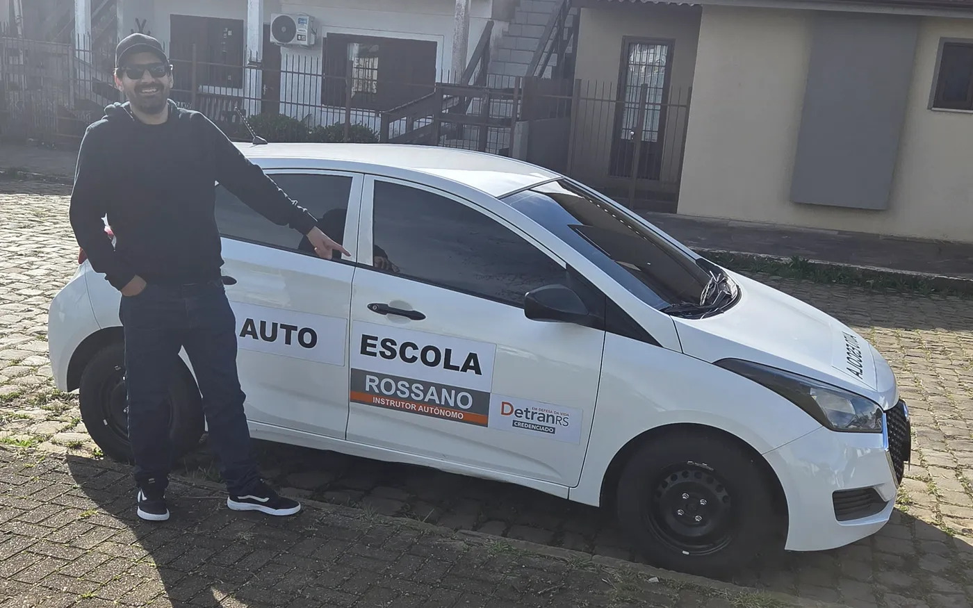 Instrutor Rossano sorrindo ao lado do carro de aula no trânsito real